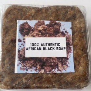 May include: A bar of dark brown African black soap wrapped in clear plastic. The label reads "100% Authentic African Black Soap".