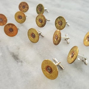 May include: A set of 10 gold-toned cufflinks featuring a round design with a center circle. The cufflinks are made from repurposed shotgun shells.