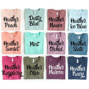 May include: Twelve different colored t-shirts with the word "Heather" and a color name printed on each shirt. The colors are peach, dusty blue, mauve, ice blue, sunset, mint, orchid, slate, raspberry, olive, maroon, and navy.