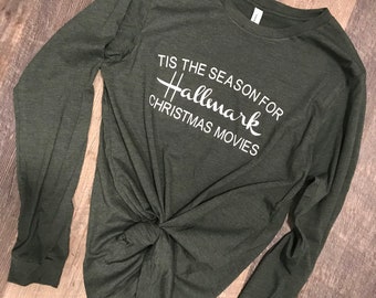 May include: A green long-sleeved t-shirt with the text "Tis the season for Hallmark Christmas Movies" printed in white.