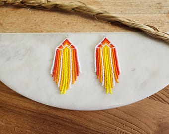 May include: A pair of orange, yellow, and white beaded earrings with a geometric design. The earrings are hanging from silver hooks.