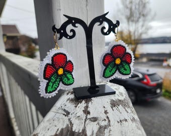 May include: A pair of beaded earrings with a red flower design on a white background. The earrings are hanging from a black stand.