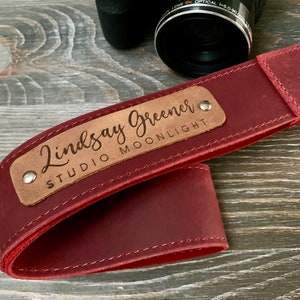 May include: A red leather camera strap with a brown leather patch that says "Lindsay Greener Studio Moonlight".