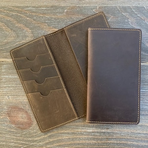 May include: A set of three brown leather wallets. One wallet is closed, one is open with card slots, and the third is partially open. All have visible stitching.