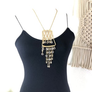May include: A gold chain necklace with a square pendant featuring a geometric design of clear glass beads. The pendant has a cascading fringe of clear glass beads.