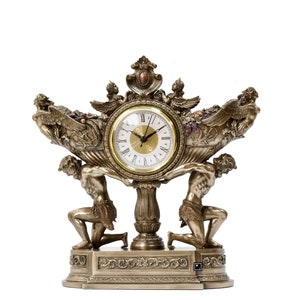 May include: A gold-toned clock with a Roman numeral face and a decorative design featuring two figures holding up a bowl with grapes and cherubs.