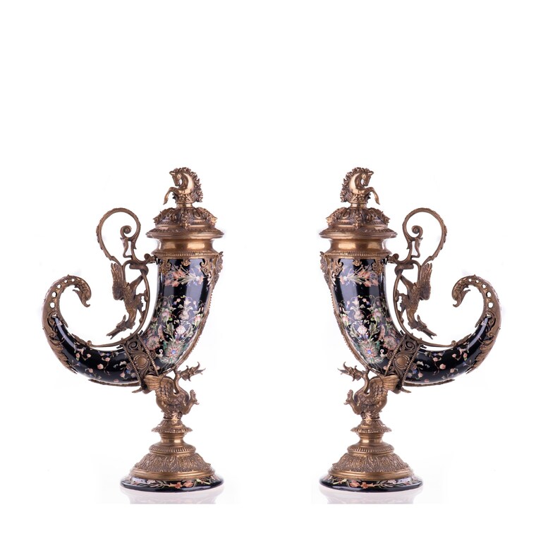 May include: Pair of ornate, black and gold decorative cornucopia vases. Each vase features a curved horn shape with floral designs, bronze accents, and a detailed base. The vases are likely for display.