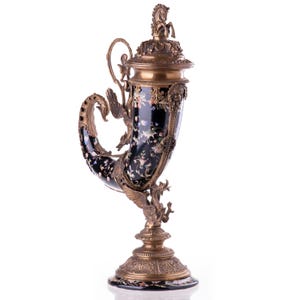 May include: An ornate, black and gold decorative horn-shaped vessel. The vessel features intricate floral and dragon designs, with a horse figurine on the lid. The base and accents are gold-toned, creating a luxurious aesthetic. A unique decorative piece.