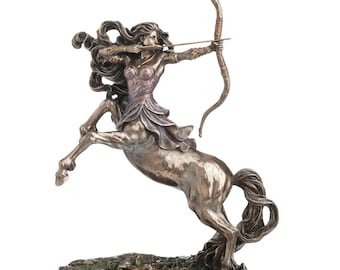 May include: A bronze-toned statue of a centauride archer in a rearing pose, holding a bow and arrow. The figure features flowing hair, a detailed bodice, and a skirt, standing on a textured base with a plaque labeled CENTAURIDES at the front.