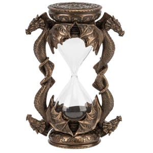 May include: Bronze-colored hourglass with a clear glass center. The hourglass is supported by two dragon figures, with intricate detailing on the dragons and the base. The top and bottom of the hourglass have decorative patterns.