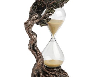 May include: A bronze-colored hourglass featuring a sculpted figure integrated into a tree trunk base and top. The figure's hair and arms extend into the branches supporting the top platform. The clear glass bulb contains fine tan sand.