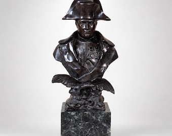 May include: A bronze bust of a historical figure wearing a bicorne hat and military attire. The sculpture features a detailed depiction of the person's face and uniform, mounted on a dark green marble block. An eagle is at the base of the bust.