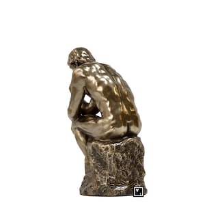 May include: A bronze sculpture of a man sitting in a contemplative pose, with his head resting on his hand. The sculpture is mounted on a rough, textured base.