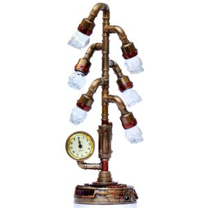 May include: Steampunk table lamp in bronze, with six clear skull-shaped bulbs. The lamp has a small clock and is made from pipes and fittings, creating an industrial aesthetic. The design is reminiscent of Victorian era technology.