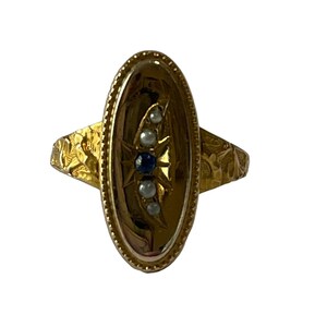 Peut inclure: Une bague en or avec un serti de forme ovale. Le serti est d&eacute;cor&eacute; d'un motif d'&eacute;toile et pr&eacute;sente un saphir bleu et quatre perles blanches.