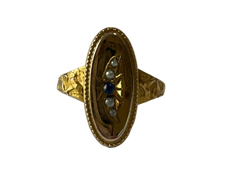 Peut inclure: Une bague en or avec un serti de forme ovale. Le serti est d&eacute;cor&eacute; d'un motif d'&eacute;toile et pr&eacute;sente un saphir bleu et quatre perles blanches.