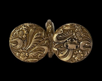 May include: A pair of gold-toned, round, hinged pocket watch covers with an intricate floral design.