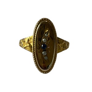 Peut inclure: Une bague en or avec une b&eacute;li&egrave;re ovale sertie d'un saphir bleu et de perles blanches. La bande de la bague est textur&eacute;e avec un motif floral.