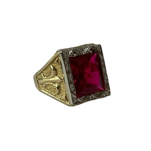 May include: A gold ring with a large, red, square-shaped gemstone set in a white gold frame. The ring has a detailed design on the band.