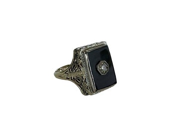 May include: A gold ring with a black onyx stone set in a square frame. The stone is accented with a small diamond in the center.
