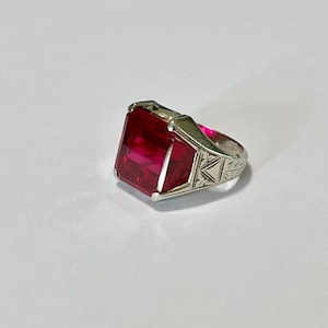 Puede incluir: Un anillo de plata con una gran piedra preciosa roja oscura de talla esmeralda.