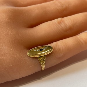 Peut inclure: Une bague en or avec une b&eacute;li&egrave;re ovale sertie de petites perles blanches et d'une seule pierre noire. La bande de la bague est textur&eacute;e.