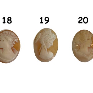 May include: Three oval-shaped cameo pendants with a carved design of a woman's profile. The cameos are made of a light brown shell material with a white carving. The cameos are numbered 18, 19, and 20.