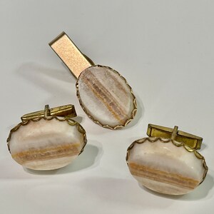 May include: A set of gold-toned cufflinks and a tie clip with oval-shaped white and brown agate stones.
