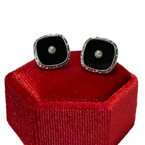 May include: A pair of black onyx cufflinks with a single pearl accent on each, set in silver and displayed in a red velvet box.