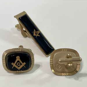 May include: A set of gold-toned cufflinks and a tie clip featuring black enamel with a gold Masonic symbol.