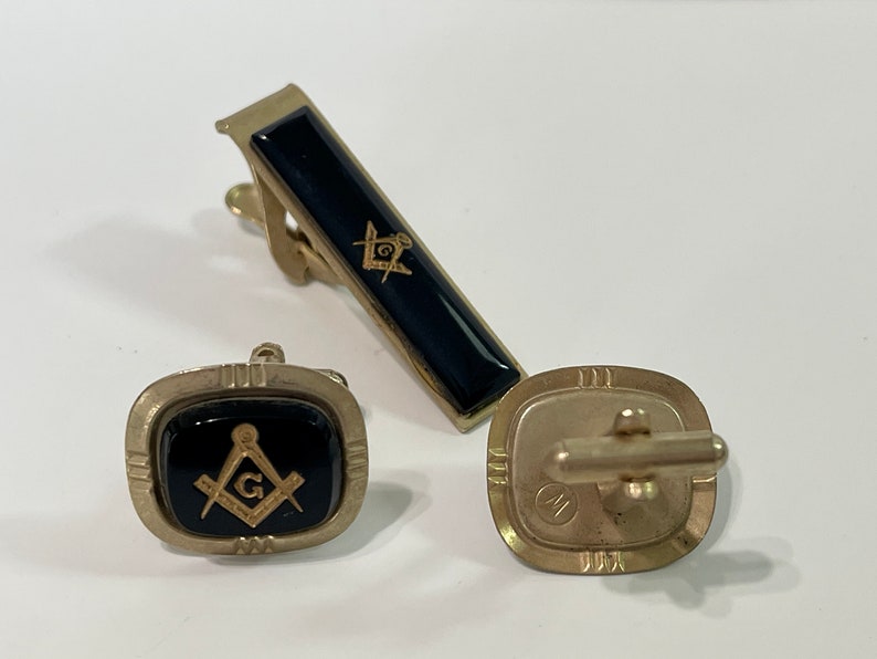 May include: A set of gold-toned cufflinks and a tie clip featuring black enamel with a gold Masonic symbol.