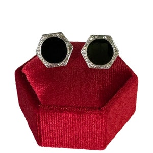 May include: A pair of black onyx earrings with a silver filigree design, displayed in a red velvet box.