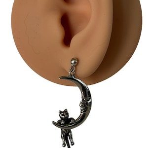 May include: Silver crescent moon earring with a small black cat figurine hanging from it.