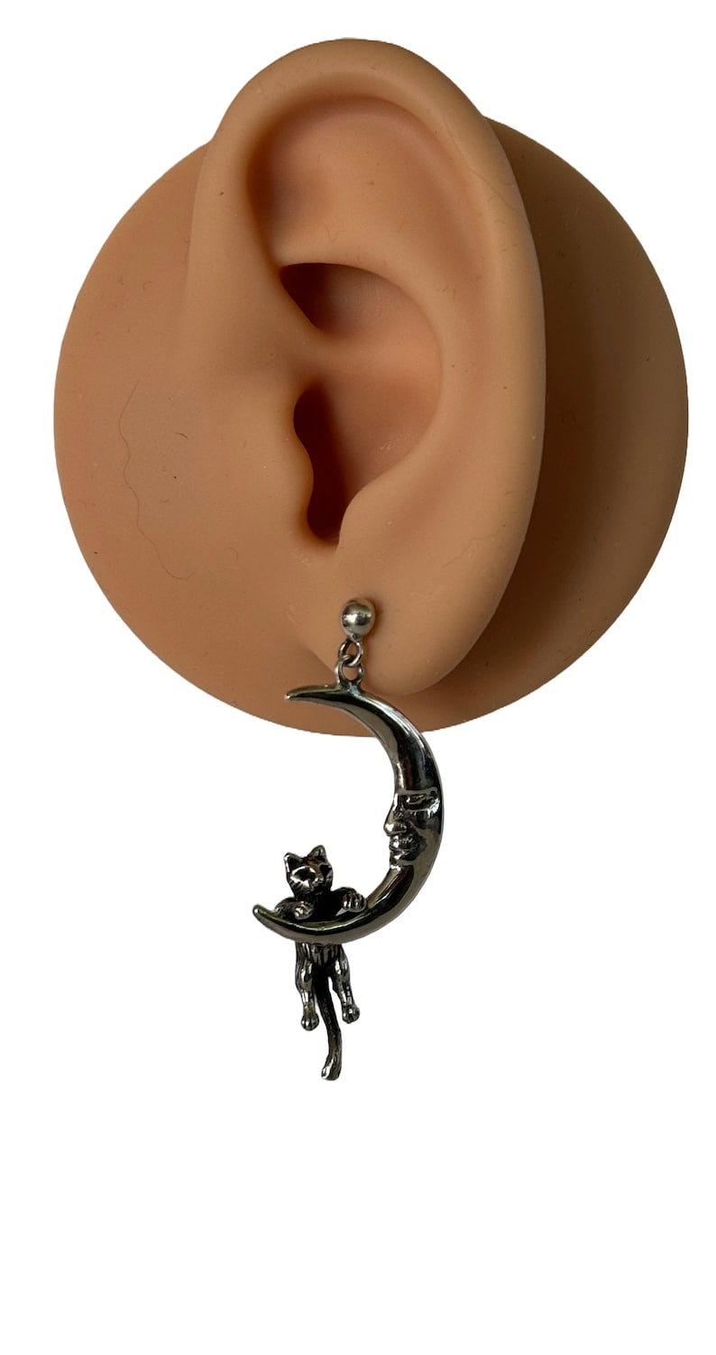 May include: Silver crescent moon earring with a small black cat figurine hanging from it.