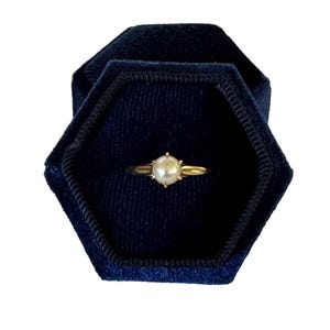May include: A gold ring with a single pearl set in the center. The ring is displayed in a blue velvet ring box.