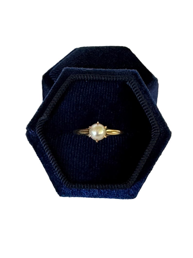May include: A gold ring with a single pearl set in the center. The ring is displayed in a blue velvet ring box.