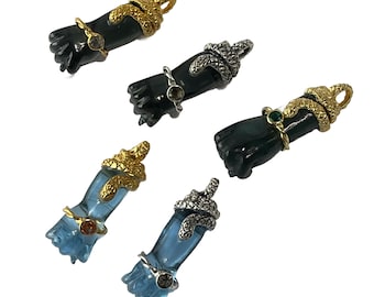 May include: Five pendants featuring a hand with a snake wrapped around it. The pendants are made of black and blue stone with gold and silver accents.