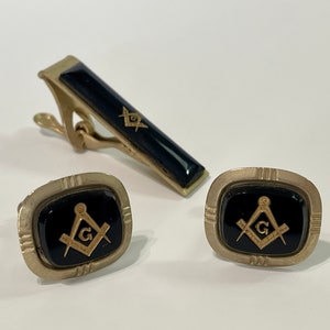 May include: A set of gold-tone cufflinks and tie bar with black enamel and a gold Masonic symbol.