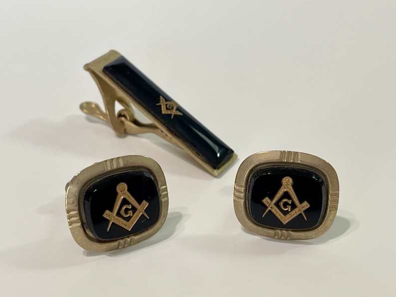 May include: A set of gold-tone cufflinks and tie bar with black enamel and a gold Masonic symbol.