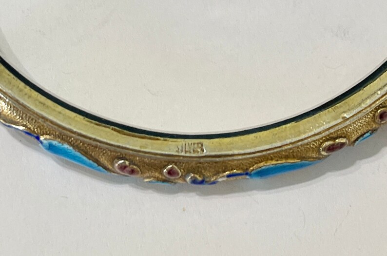 K&ouml;nnte beinhalten: Ein silbernes Armreif-Armband mit blauen und roten Emaildetails. Das Armband ist innen mit "SILVER" gekennzeichnet.