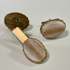 May include: A pair of gold cufflinks with oval-shaped white and brown agate stones set in a gold filigree frame.