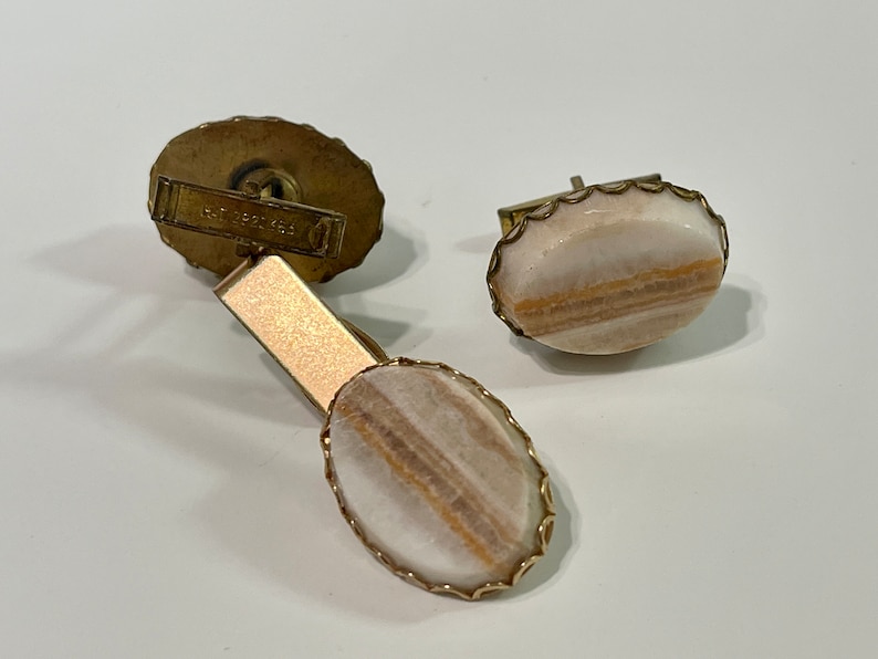 May include: A pair of gold cufflinks with oval-shaped white and brown agate stones set in a gold filigree frame.