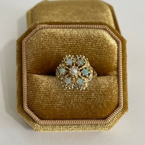 May include: A gold ring with a flower design set with opals and a pearl in the center. The ring is in a velvet ring box.