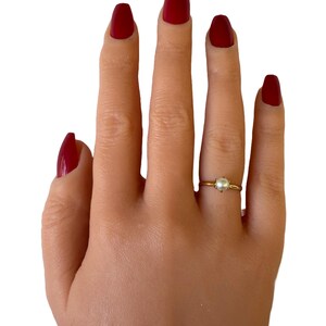 May include: A gold ring with a single white pearl on a hand with red nail polish.