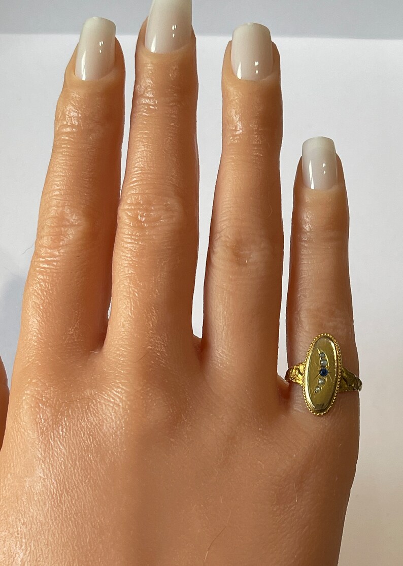 Peut inclure: Une bague en or avec un chaton de forme ovale serti d'une pierre bleue et de petites pierres blanches. La bague a une bande textur&eacute;e et d&eacute;taill&eacute;e.