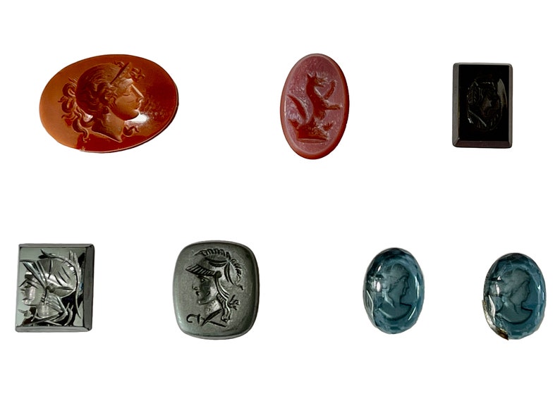 Op de afbeelding: Zes antieke cameo-intagli, waaronder een rode karneol met een vrouwelijk profiel, een rode karneol met een leeuw, een zwarte onyx met een vrouwelijk profiel, een zwarte onyx met een vrouwelijk profiel, een grijze steen met een vrouwelijk profiel en twee blauwe stenen met een vrouwelijk profiel.