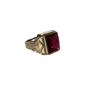 May include: A gold ring with a square, faceted, dark red gemstone.