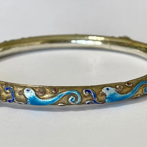 K&ouml;nnte beinhalten: Ein silbernes Armreif-Armband mit blauen und wei&szlig;en Emaildetails und zwei roten Korallenakzenten.