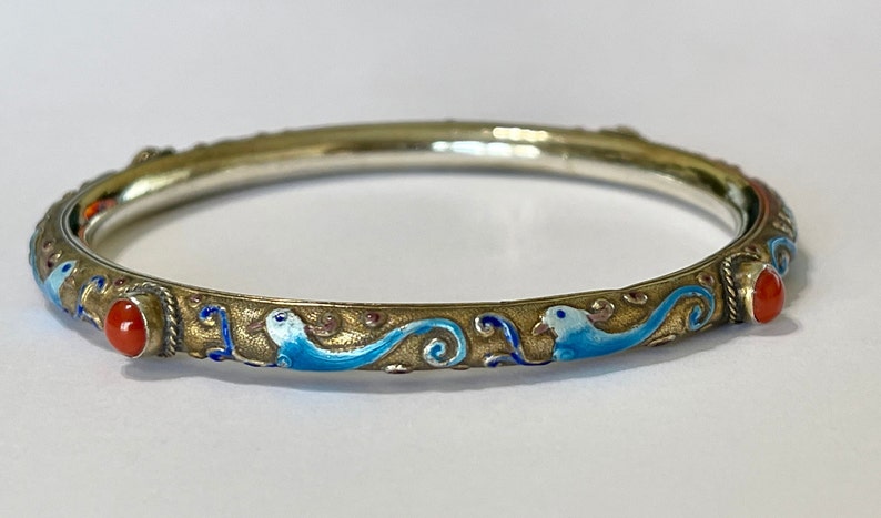 K&ouml;nnte beinhalten: Ein silbernes Armreif-Armband mit blauen und wei&szlig;en Emaildetails und zwei roten Korallenakzenten.