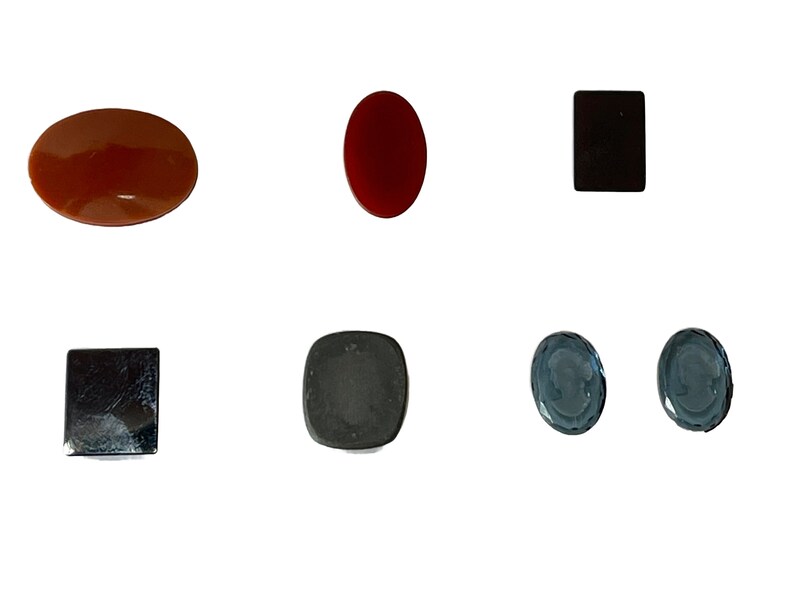 Op de afbeelding: Assortiment van zes ovale en vierkante cabochon edelstenen. De edelstenen zijn in tinten rood, bruin, zwart en blauw.